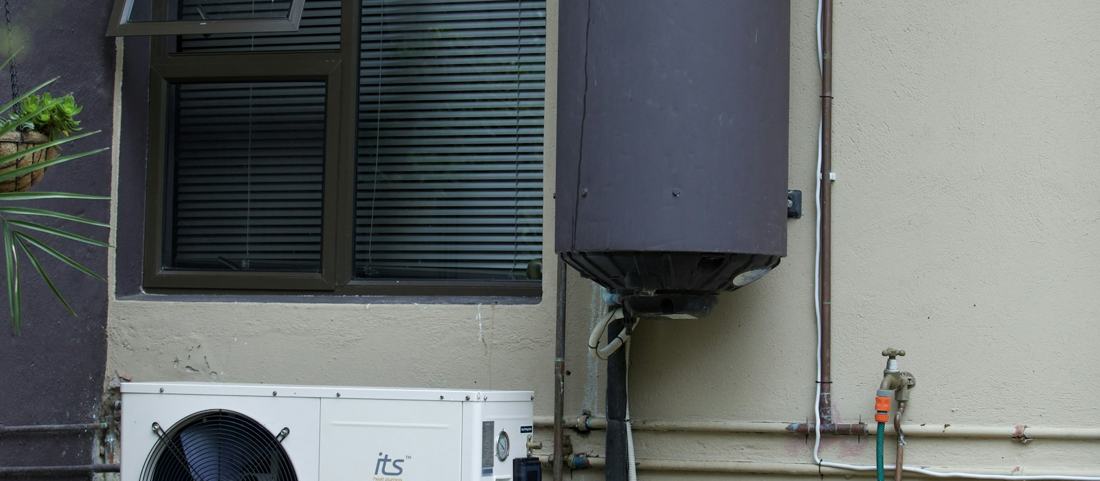 An outdoor hot water tank and heat pump on a house wall